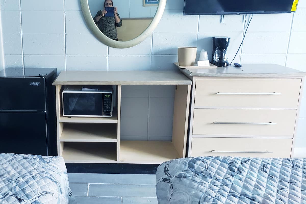 A bedroom with two beds, a desk with a computer, a microwave, a coffee maker, and a mirror on the wall.