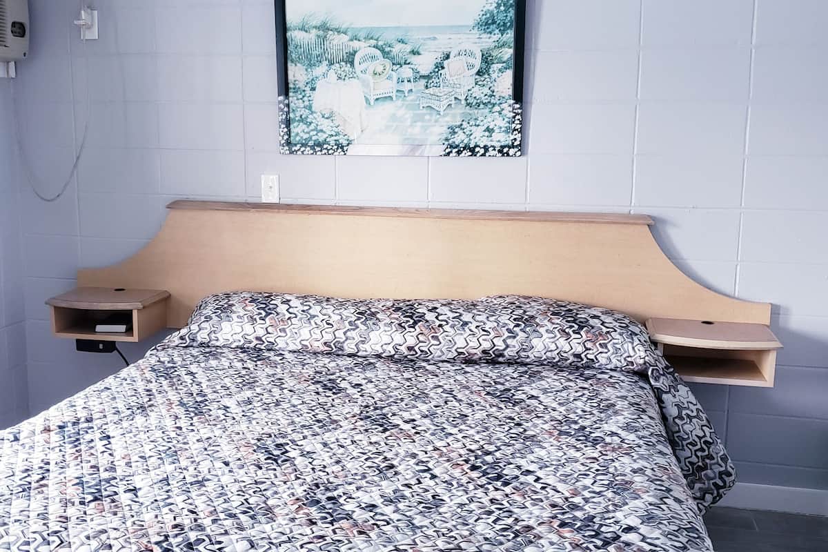A bedroom with a bed, a headboard, a nightstand, a wall-mounted air conditioner, and a framed picture on the wall.