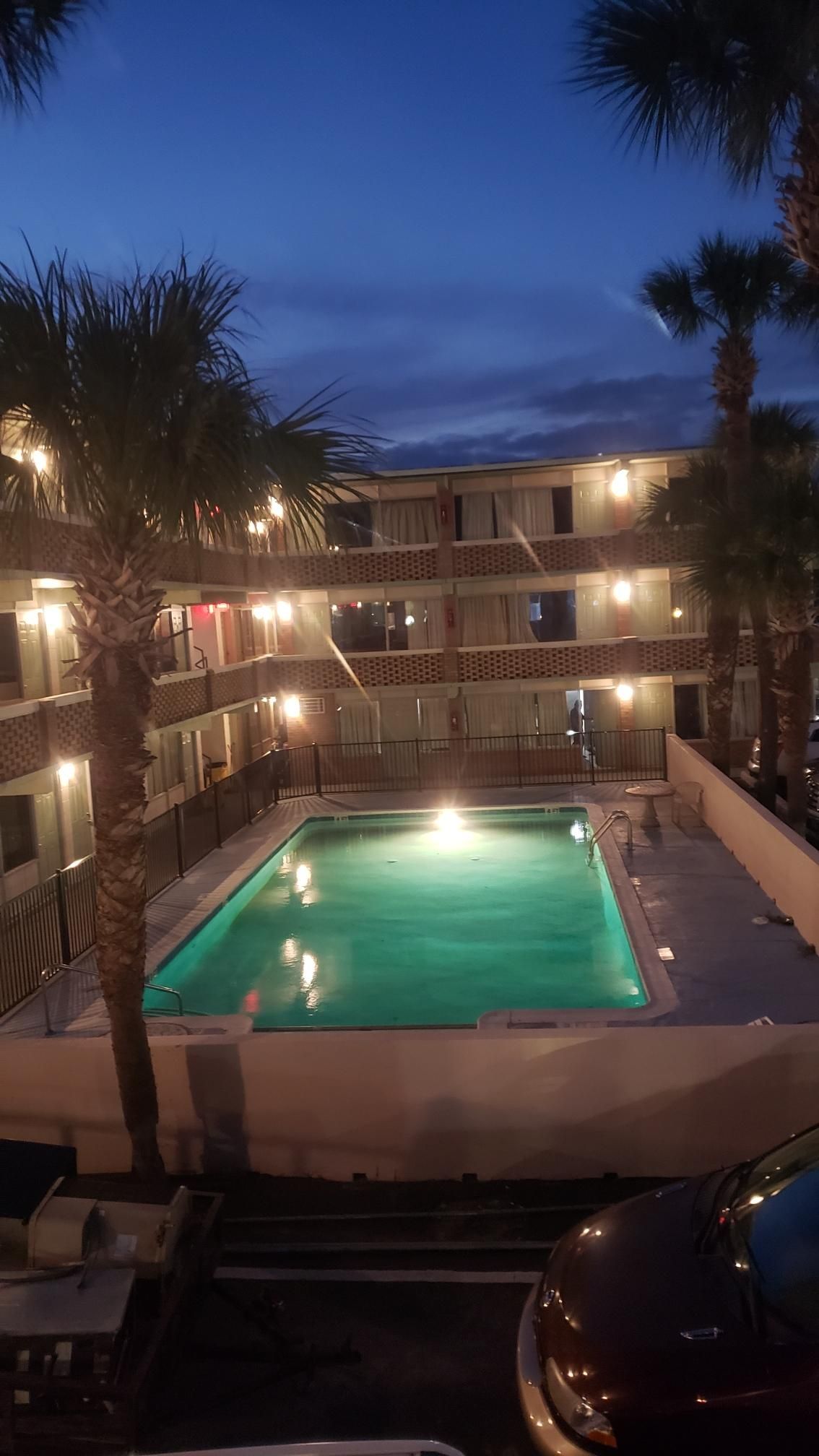 A hotel with a swimming pool, multiple balconies, and palm trees.