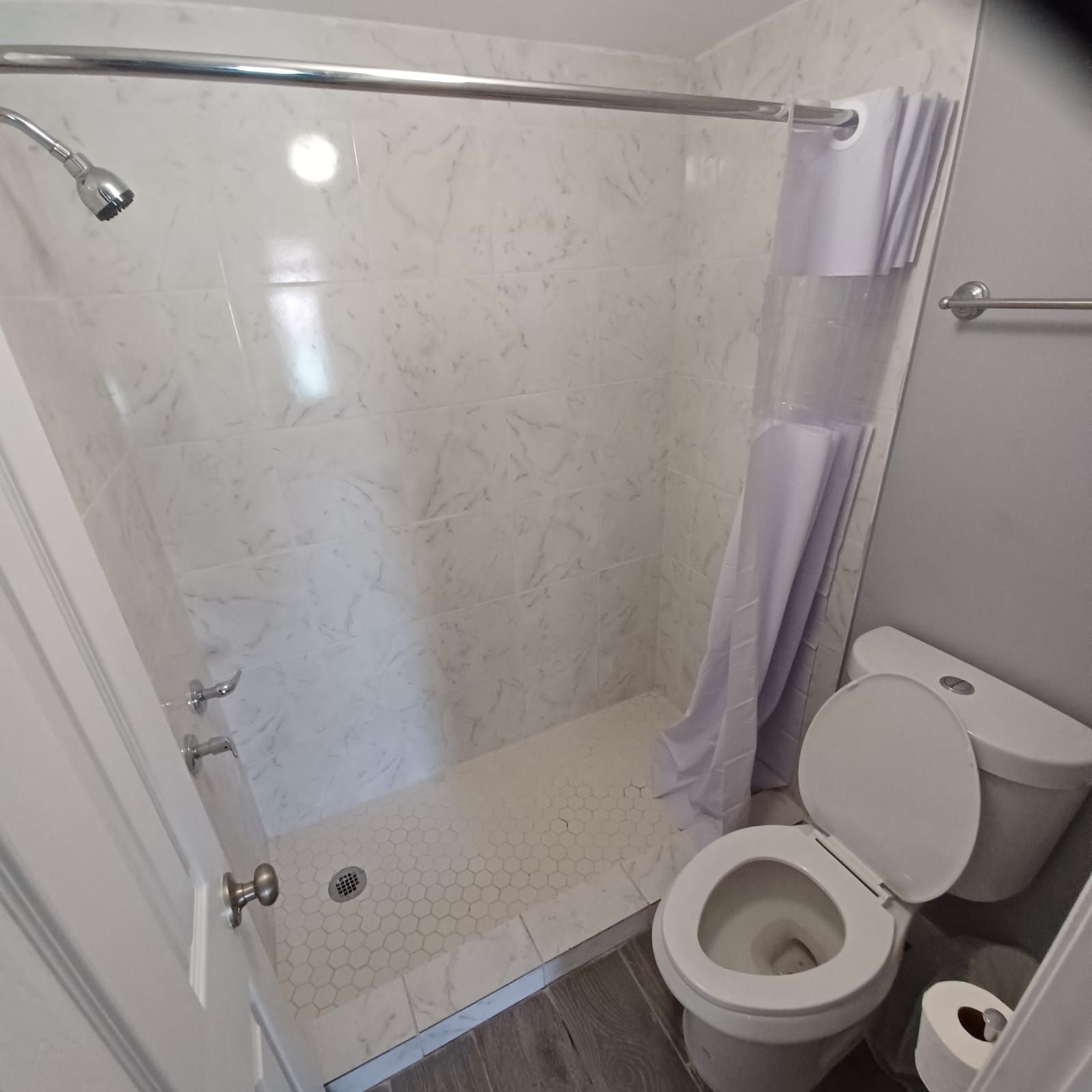 A bathroom with a shower, toilet, and a glass door.