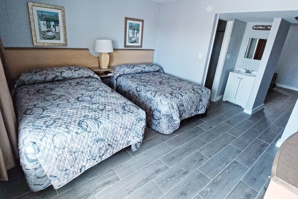 A hotel room with two beds, a nightstand, a lamp, and a small cabinet.