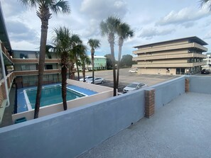 A pool area with palm trees, a parking lot, and a multi-story building with a patterned facade.