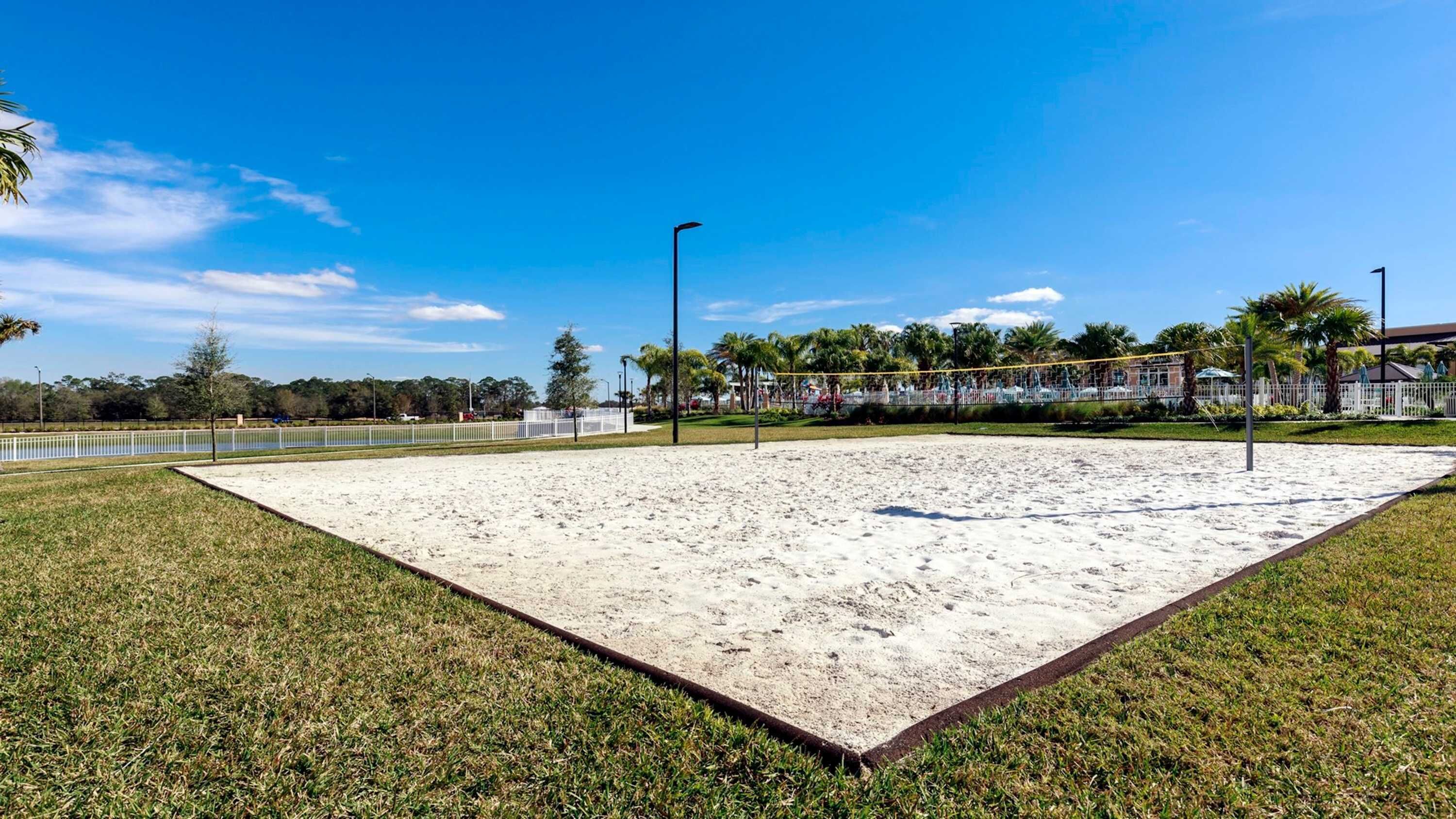 En sandvolleyspårplan med ett vitt staket, omgiven av gräs och palmer.