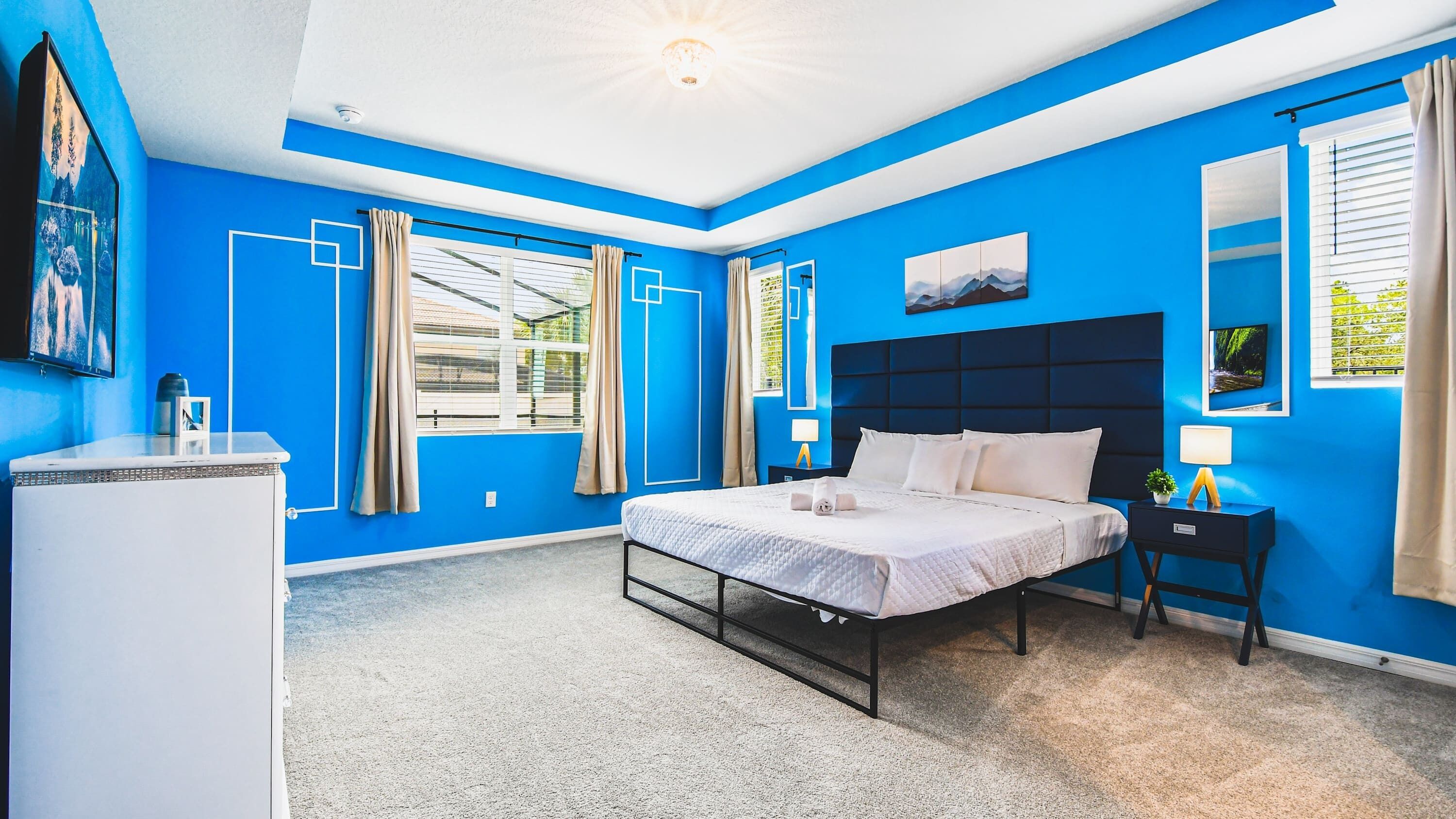 A modern bedroom with a large bed, a nightstand, a desk, and a window with curtains.