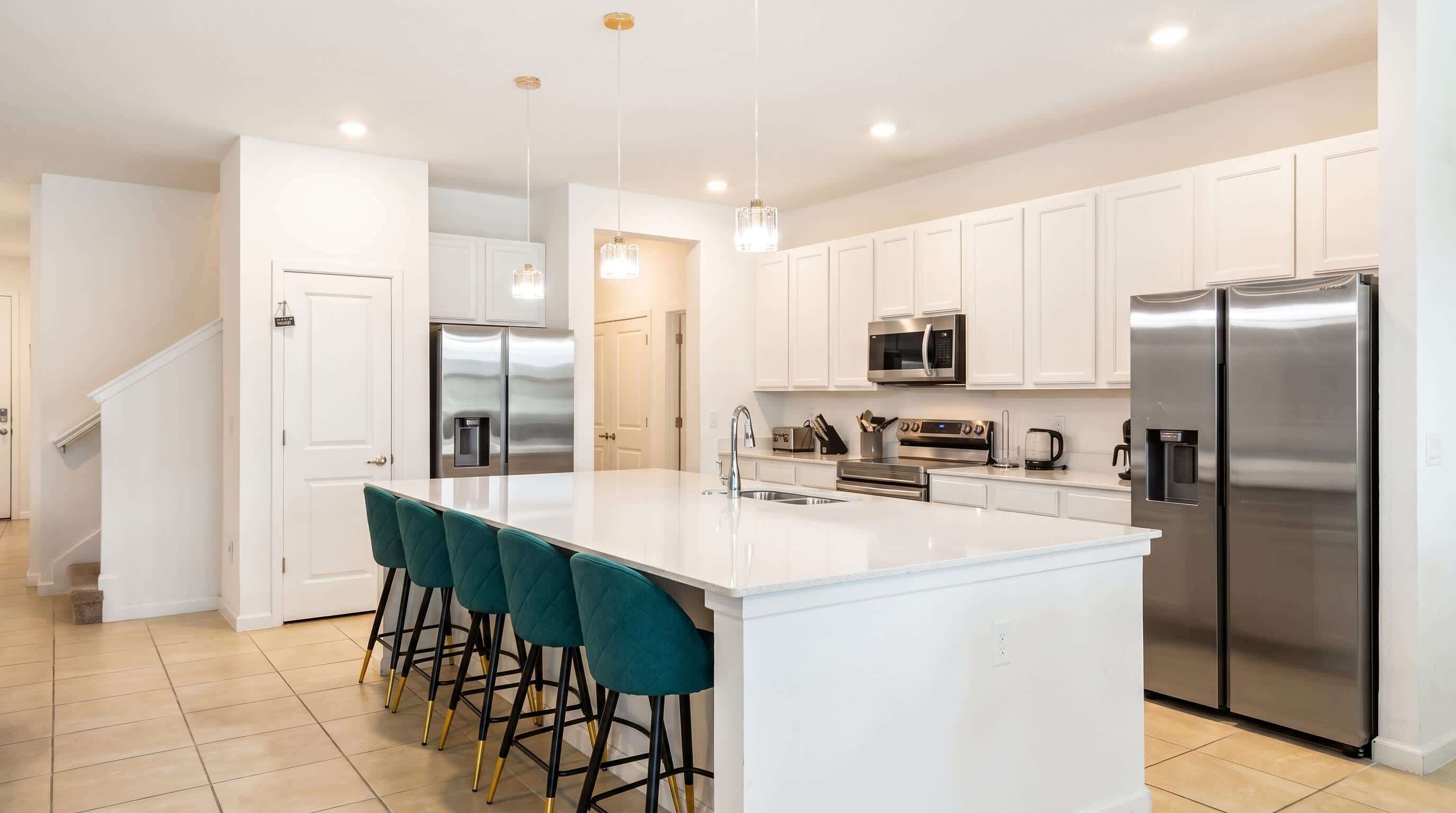 A modern kitchen with white cabinetry, stainless steel appliances, a central island with bar stools, and pendant lighting.