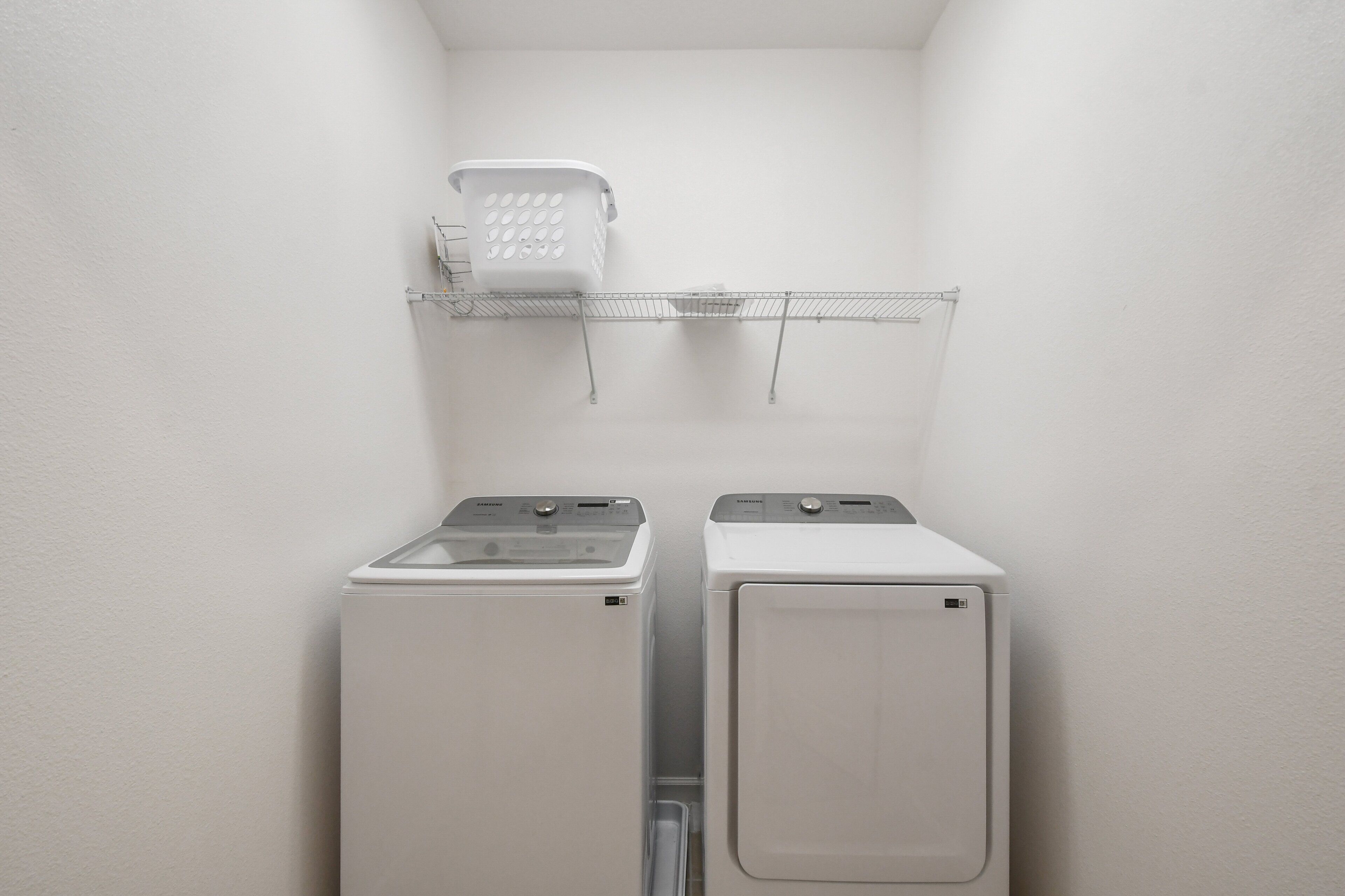 A laundry area with two stacked washing machines and a drying rack above.