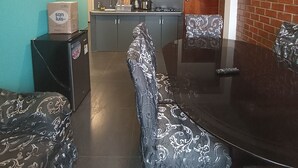 Ein Essbereich mit einem dunklen Holztisch und gemusterten Stühlen, im Hintergrund eine Küche und eine wandfarben türkise Wand.