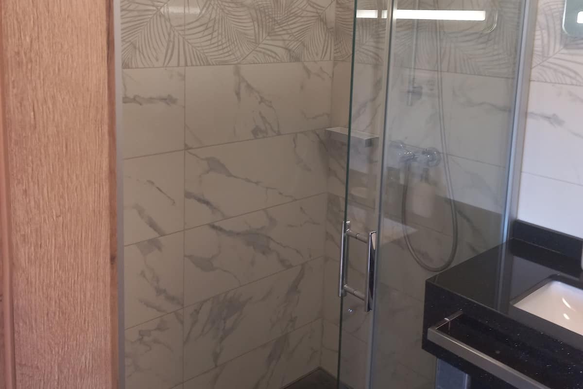 A bathroom with a glass shower enclosure, marble-patterned walls, and a black countertop.