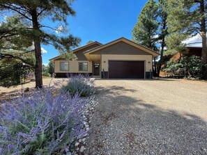 Una casa a due piani con garage, circondata da alberi e un vialetto sterrato.