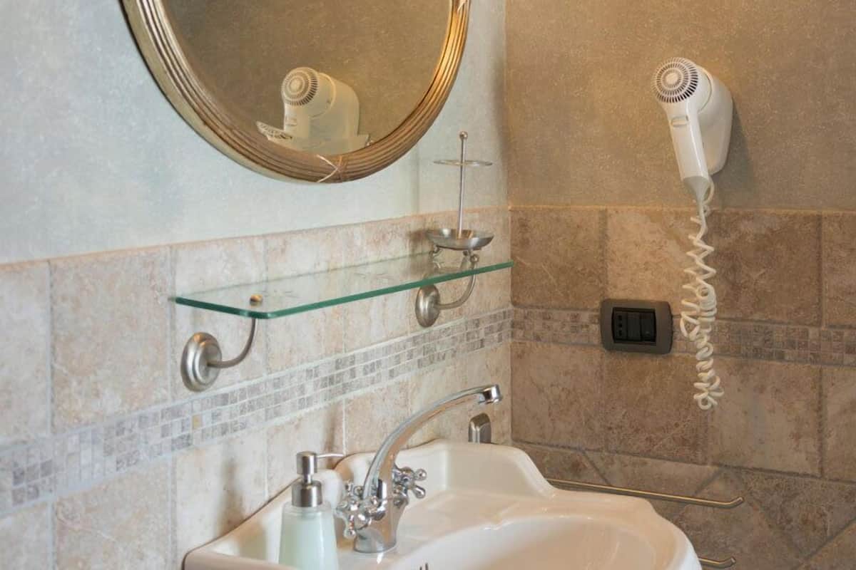 A bathroom with a large mirror, a sink, a hairdryer, and a glass shelf.
