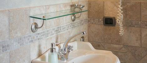 A bathroom with a large mirror, a sink, a hairdryer, and a glass shelf.