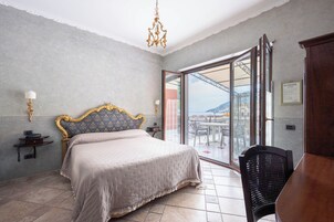Un dormitorio con una cama grande, una araña, una mesita de noche y vistas a un balcón con mesa y sillas.