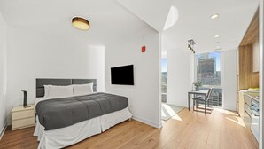 Une chambre moderne avec un grand lit, une table de chevet, une télévision et un balcon offrant une vue sur la ville.