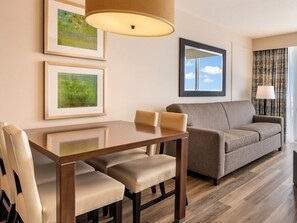 Habitación de hotel con una mesa de comedor, dos sillas, un sofá y un ventanal con vistas.