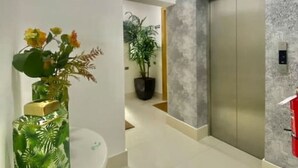 A modern elevator with a metallic finish, a white wall with a textured pattern, and a potted plant in the background. - Cozy 1BR condo w/ King bed, full AC, WiFi, smart TVs & Full kitchen in El Vergel (Santo Domingo)