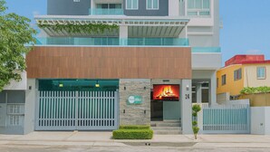 A multi-story hotel with a modern design, featuring balconies, a covered entrance, and a visible fire feature. - Cozy 1BR condo w/ King bed, full AC, WiFi, smart TVs & Full kitchen in El Vergel (Santo Domingo)