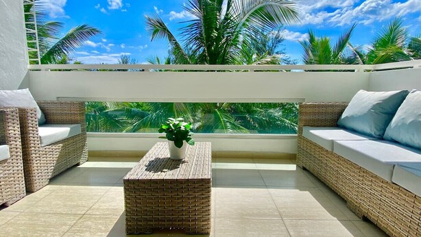 Un balcón con mobiliario de mimbre, una planta en maceta y vistas a palmeras.