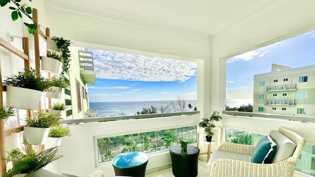 Un balcón con mobiliario de mimbre, plantas en macetas y vista al mar.