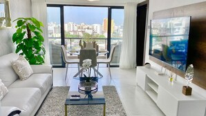Una sala de estar moderna con sofá, mesa de centro, televisor y un amplio ventanal con vistas a la ciudad.
