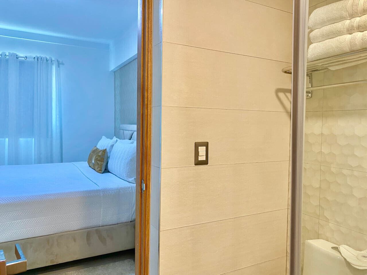 A bedroom with a bed, a bedside table, a nightstand, and a wall-mounted light switch.