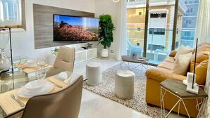 Ein modernes Wohnzimmer mit Flachbildfernseher, einem Essbereich mit Glastisch und einem Sofa mit Blick auf die Stadt.