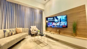 A modern living room with a sofa, a glass coffee table, a TV mounted on the wall, and a ceiling fan.