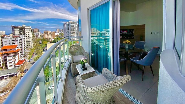 A balcony with wicker furniture, a table with a vase of flowers, and a view of the cityscape.