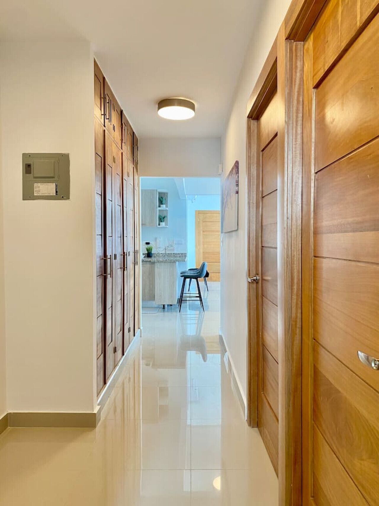 A hallway with wooden doors, a tiled floor, and a kitchen area visible in the distance.