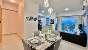 Ein moderner Essbereich mit einem Marmortisch, gedeckt für vier Personen, einer Küche im Hintergrund und einem Balkon mit Blick.