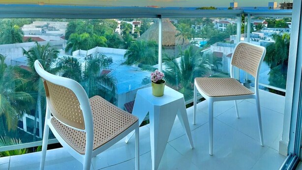 Ein Balkon mit zwei Korbstühlen und einem kleinen Tisch, mit Blick auf eine Stadtlandschaft aus Gebäuden und Grünflächen.