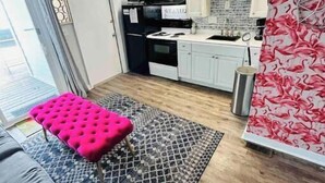 A compact living space with a kitchenette, a grey sofa, a patterned rug, and a pink ottoman. - Sunrise, Sunburn, Sunset, Repeat (Destin)
