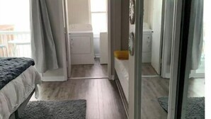 A bedroom with a bed, a small rug, a sliding glass door, and a view of a bathroom and kitchen area. - Sunrise, Sunburn, Sunset, Repeat (Destin)