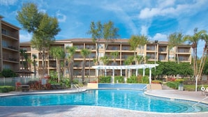 Un hotel con piscina, varios balcones y una zona cubierta con pérgola.