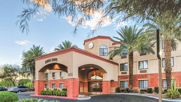 Un hotel con fachada color beige, detalles en ladrillo rojo y una entrada destacada con arcos.