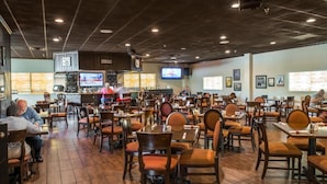 Un restaurante con varias mesas y sillas, una zona de bar con televisor y una barra.