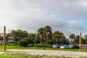 A beach volleyball court with a net, surrounded by sand, palm trees, and parked cars. - Kissimmee | Family Theme Park Stay | Pool + Hot Tub | 2BR (Kissimmee)