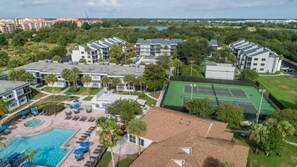 A residential complex with multiple apartment buildings, a swimming pool, tennis courts, and surrounding greenery. - Kissimmee | Family Theme Park Stay | Pool + Hot Tub | 2BR (Kissimmee)