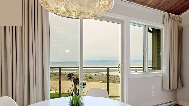 A room with a white table, a potted plant, and a view of the beach through large windows. - Oceanfront Studio with Loft - amazing views! (Qualicum Beach)