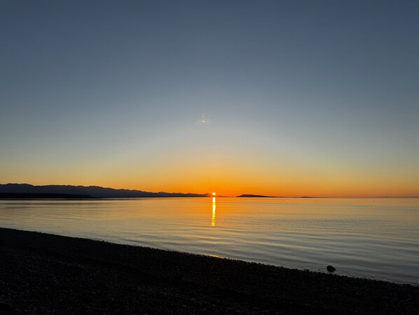 A sunset over a calm sea with a rocky shoreline. - Oceanfront Studio with Loft - amazing views! (Qualicum Beach)