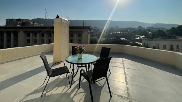 A rooftop terrace with a round glass table and four chairs, overlooking a cityscape with buildings and mountains in the distance. - Luxury apartment on av. Melikishvili with huge balcony, city center  (T'bilisi)