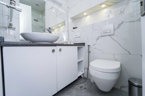 A modern bathroom with a white sink, toilet, and marble walls.
