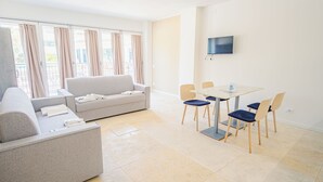 Ein modernes, gut beleuchtetes Wohnzimmer mit einer Couch, einem Esstisch mit Stühlen und einem flachbildfernseher an der Wand.