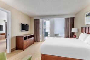 A hotel room with a bed, a TV, a desk, and a view of the outside.
