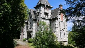 Un edificio de piedra grande con un techo empinado, varias chimeneas y una torre con balcón.