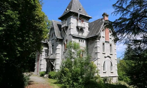 Un edificio de piedra grande con un techo empinado, varias chimeneas y una torre con balcón.