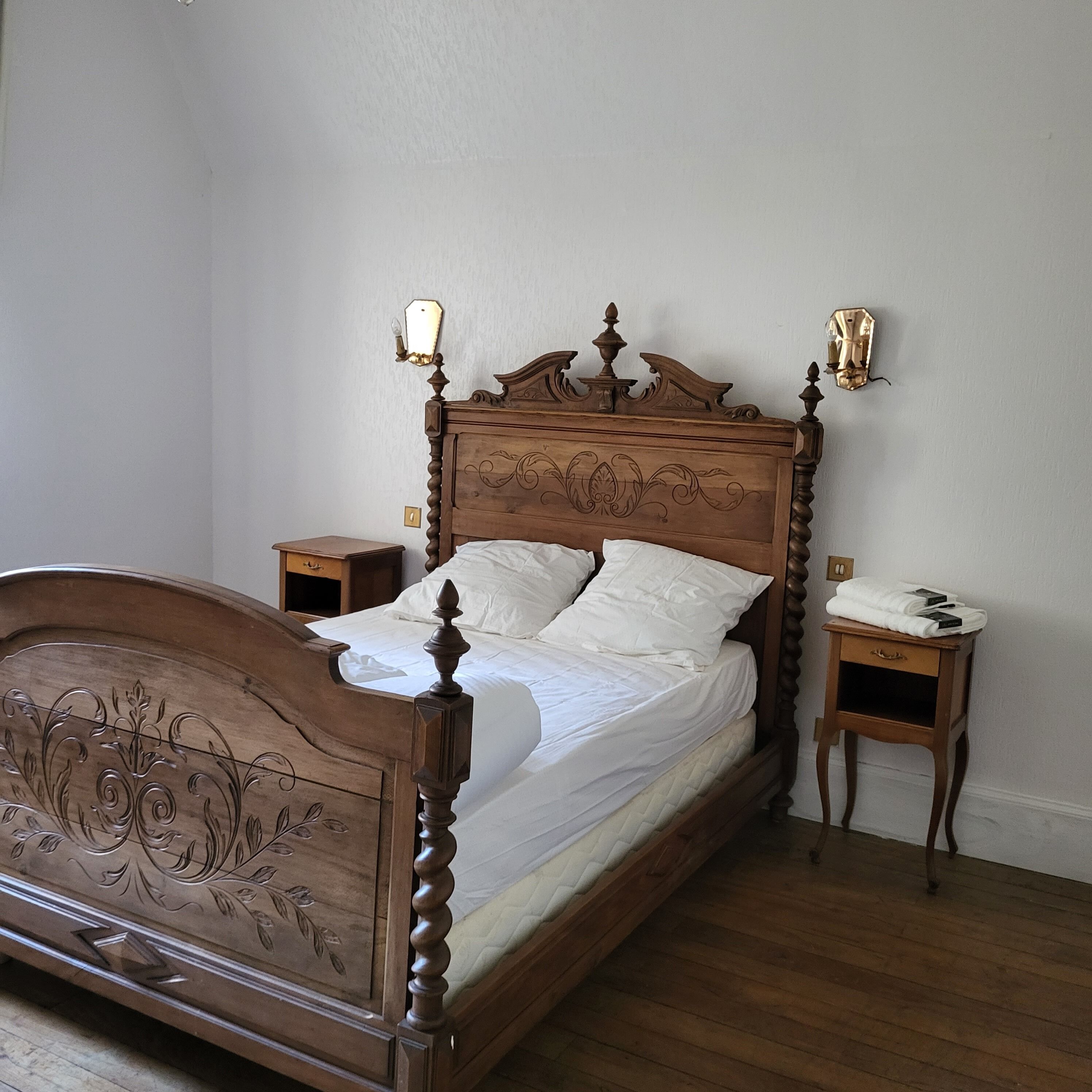 A wooden four-poster bed with a white bedspread and pillows, flanked by two nightstands with lamps.