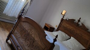Un dormitorio con cama de madera, mesita de noche, candelabro y ventana con cortinas de gasa.