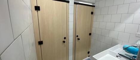 A bathroom with two wooden doors, a white sink with a blue soap dispenser, and white tiled walls.