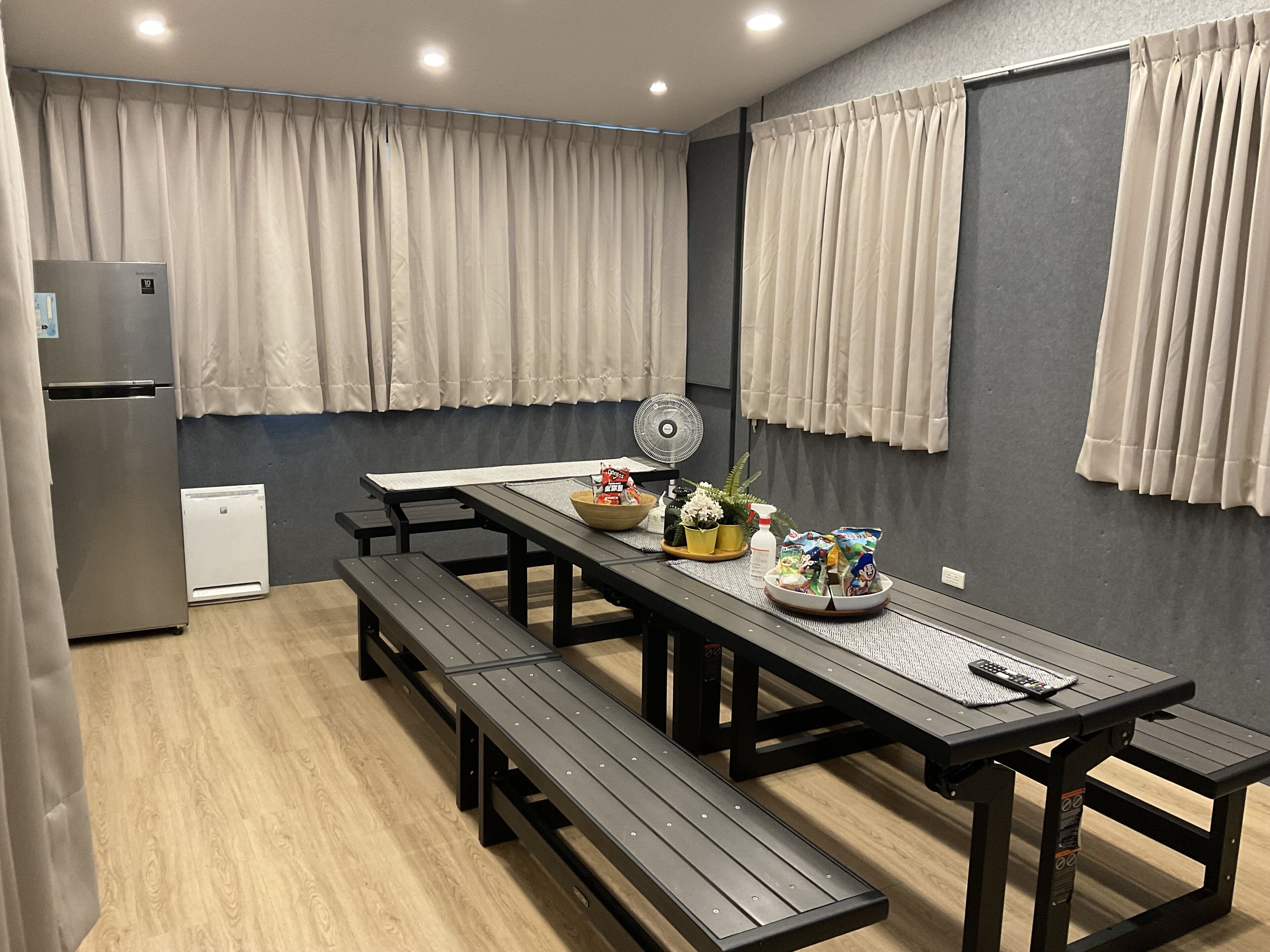A modern kitchen with a dining table, benches, a refrigerator, and a small fan.