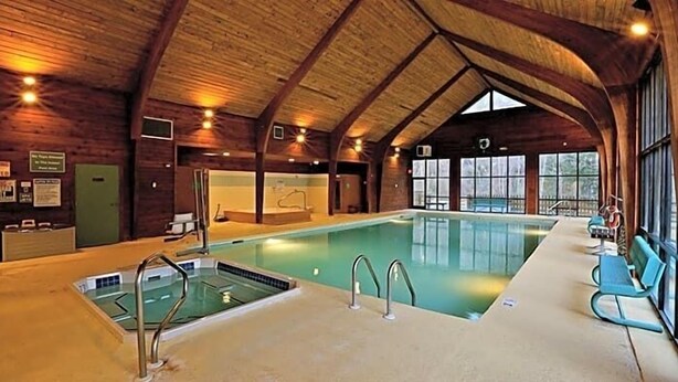 An indoor swimming pool with a wooden ceiling, a changing room, and a reception area.